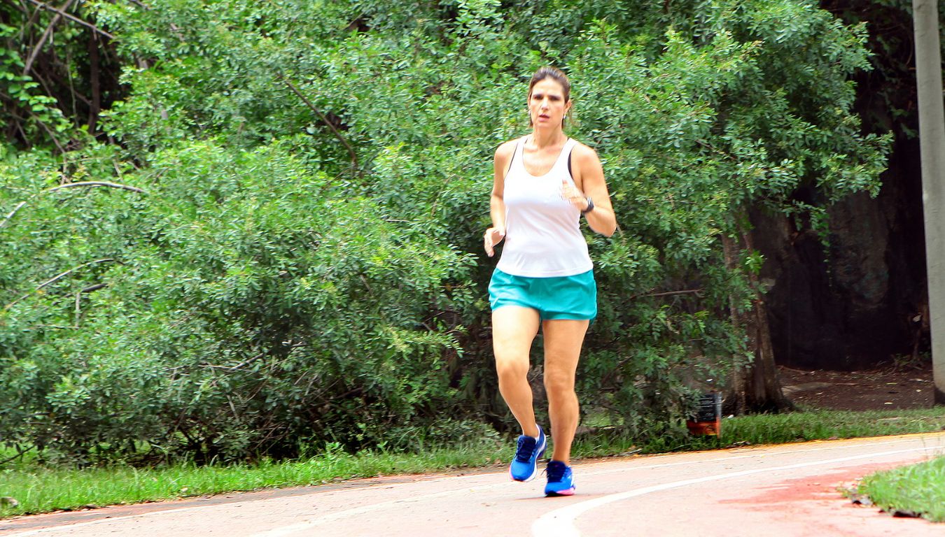 Alê Junqueira corre numa pista de atletismo com camiseta branca, sem mangas, e short azul